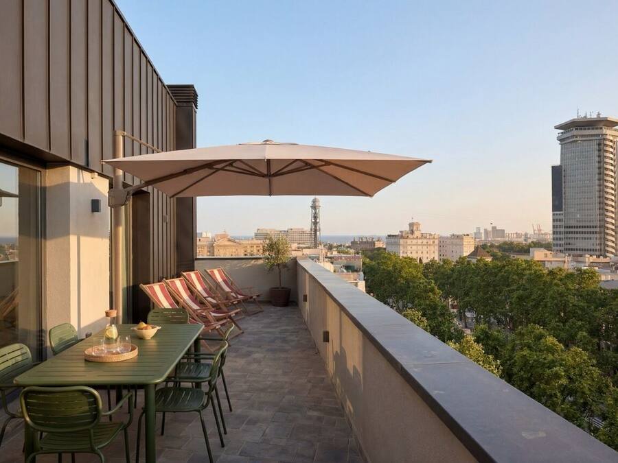 A rooftop terrace with a table, chairs, and an umbrella, overlooking a cityscape.