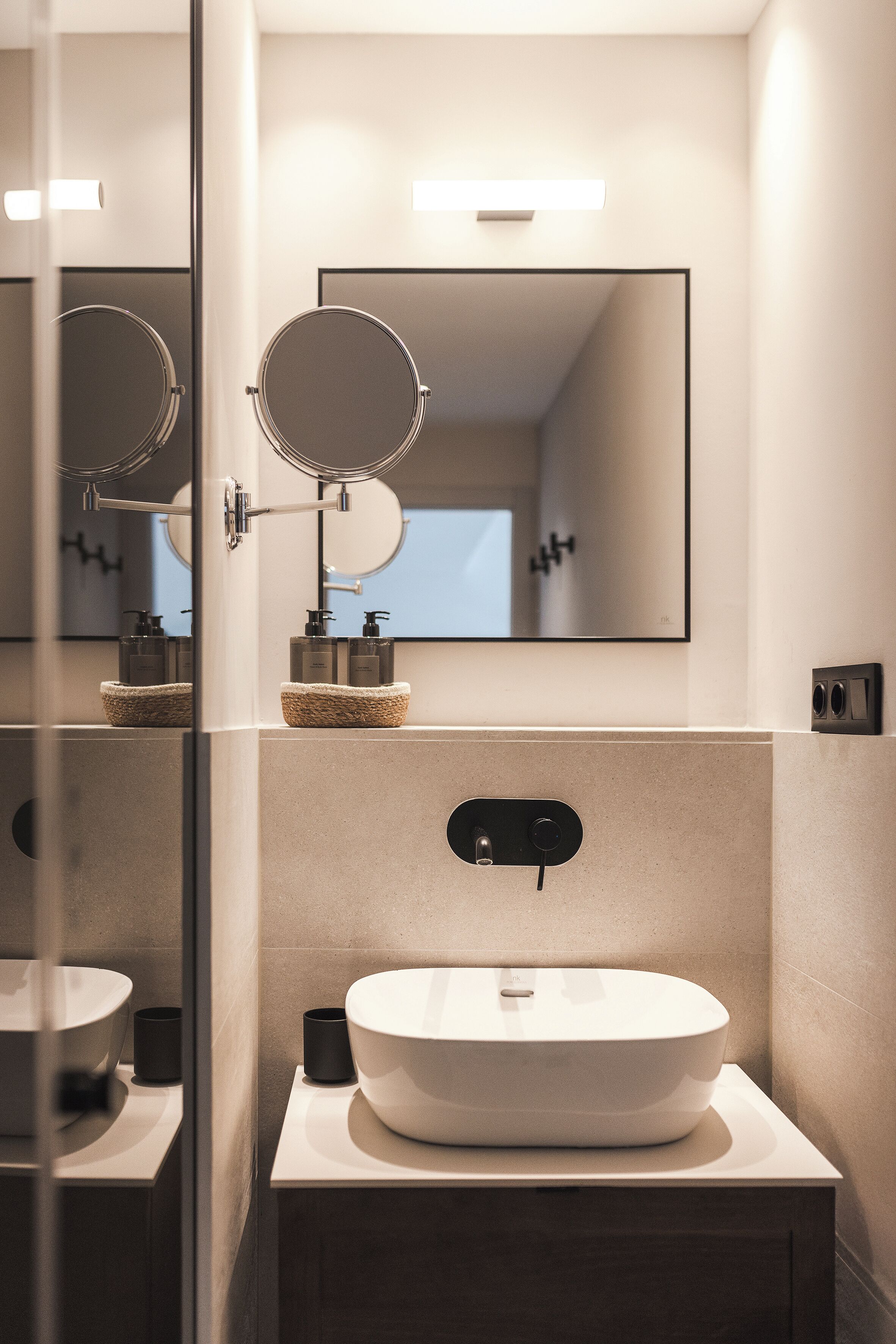 Un baño moderno con un espejo grande, un lavamanos redondo y un pequeño espejo circular sobre el lavamanos.