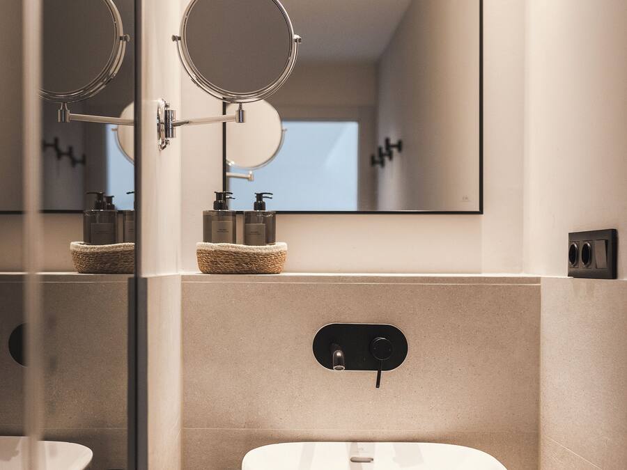 Un baño moderno con un espejo grande, un lavamanos redondo y un pequeño espejo circular sobre el lavamanos.