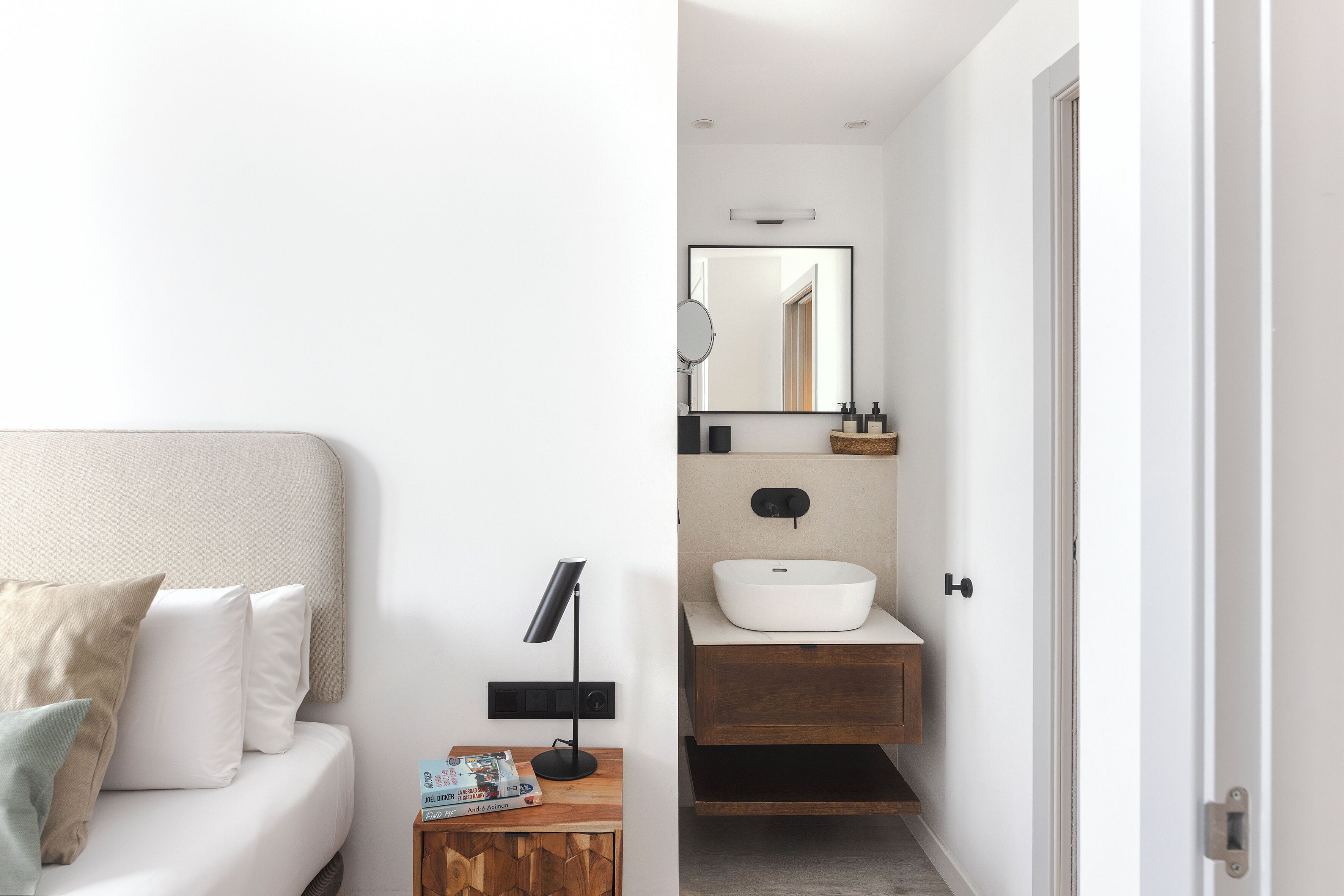 A modern bedroom with a bed, bedside table, and a nightstand with a lamp.