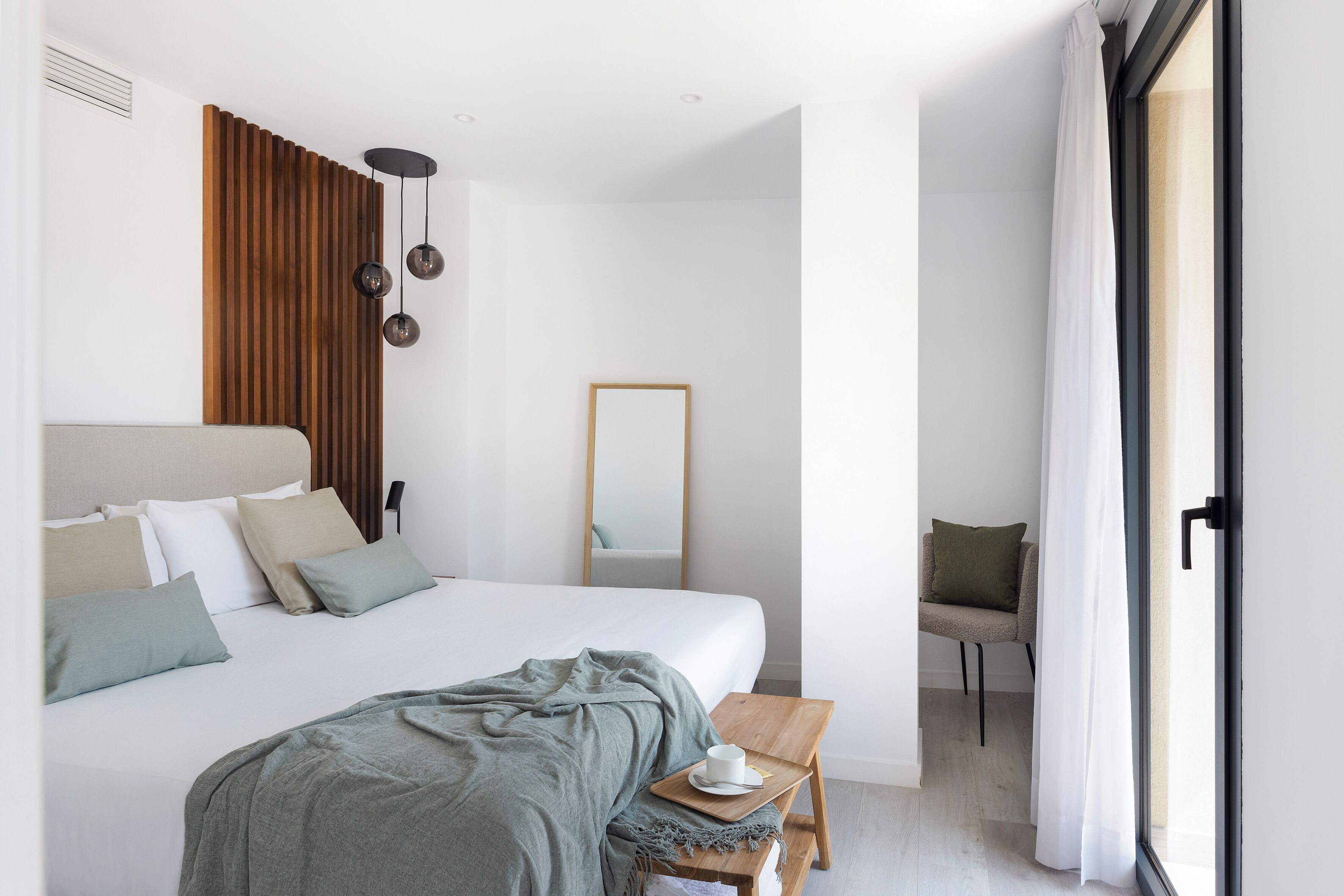 Ein modernes Hotelzimmer mit einem großen Bett, einem hölzernen Kopfteil, einem kleinen Holztisch mit einer Tasse und einem Stuhl.
