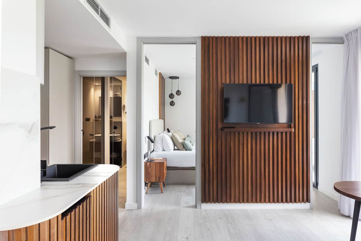 Quarto moderno com uma televisão grande, painel de parede de madeira e mesa de cabeceira com abajur.