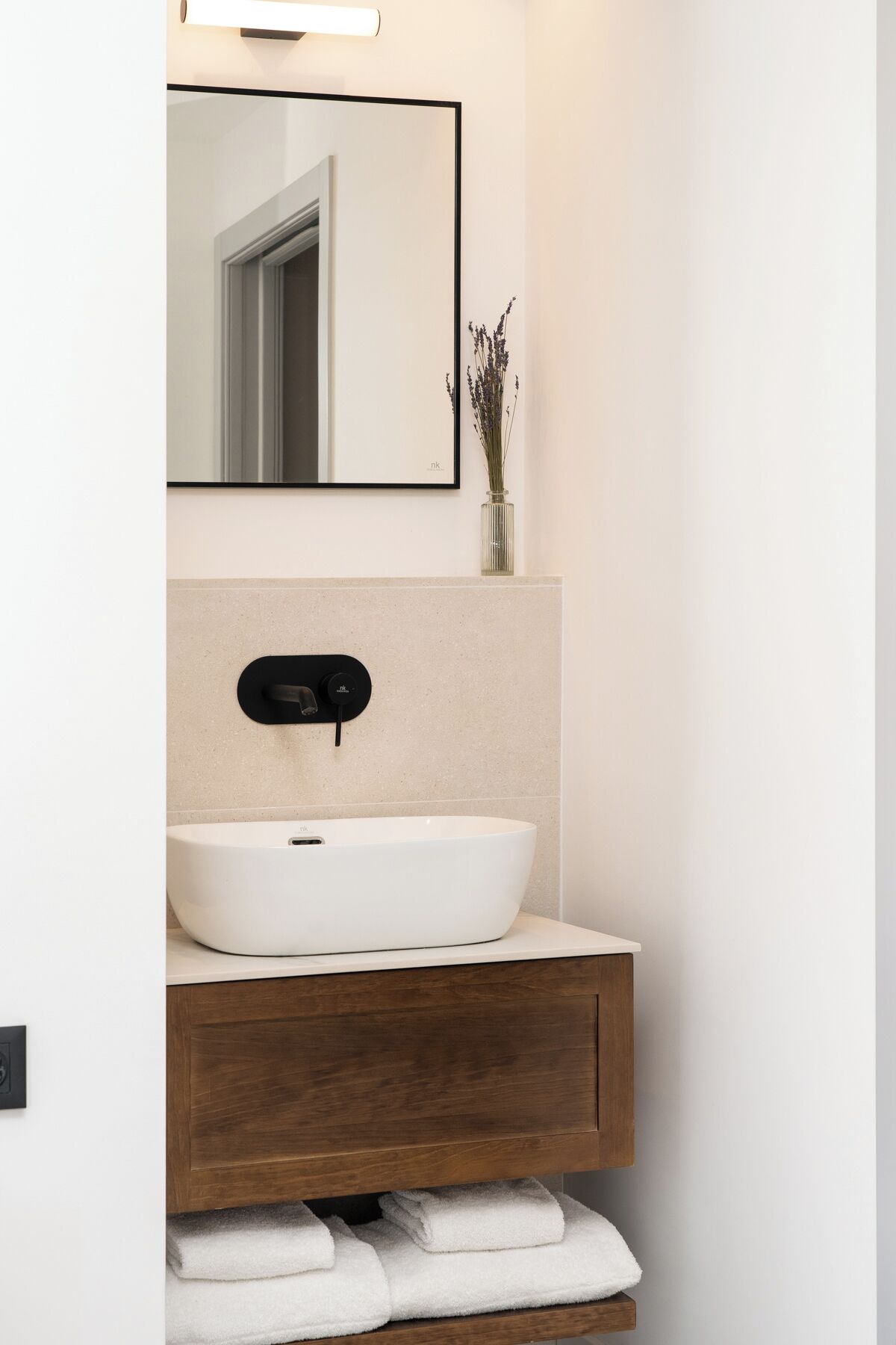 Un baño moderno con un lavamanos blanco tipo recipiente, un mueble de tocador de madera, un espejo y un florero con flores secas.