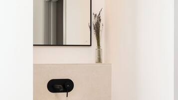 Un baño moderno con un lavamanos blanco tipo recipiente, un mueble de tocador de madera, un espejo y un florero con flores secas.