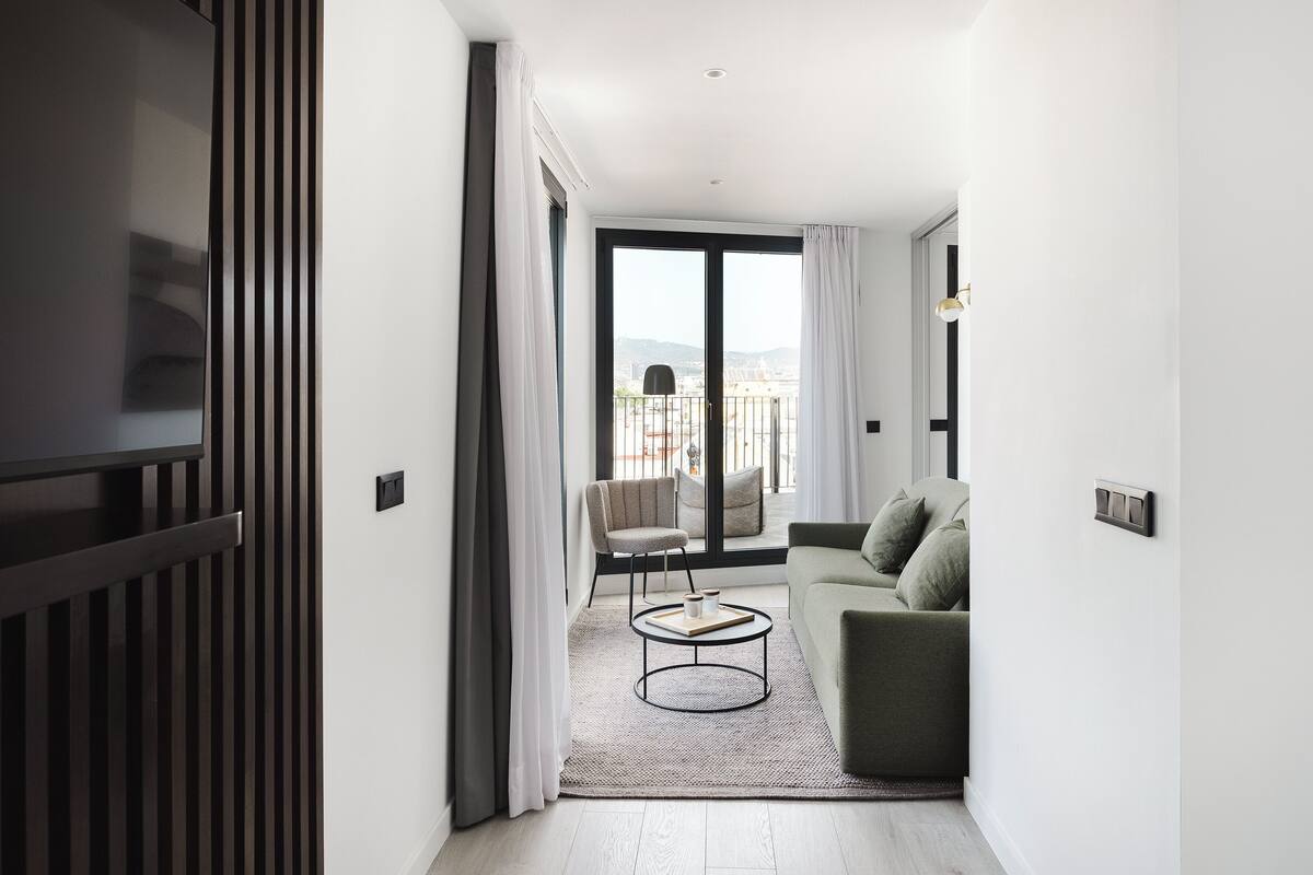 Uma sala de estar moderna com um sofá, uma mesinha redonda e vista para o exterior por uma grande janela.