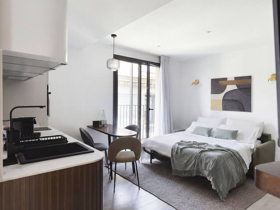 Una habitación de hotel moderna con cama, escritorio, silla y kitchenette.