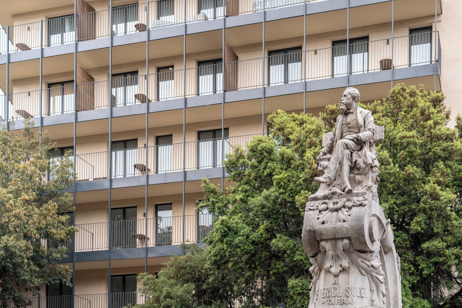 A multi-story building with balconies and a statue in the foreground.