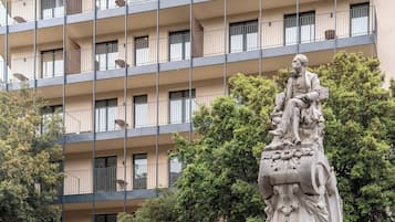 A multi-story building with balconies and a statue in the foreground.