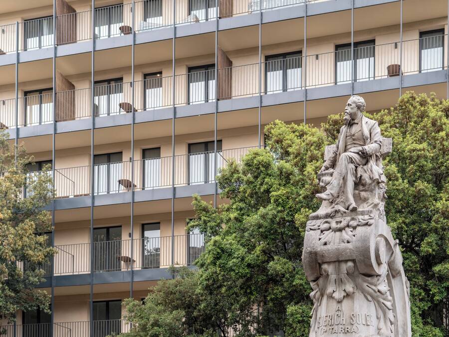 A multi-story building with balconies and a statue in the foreground.