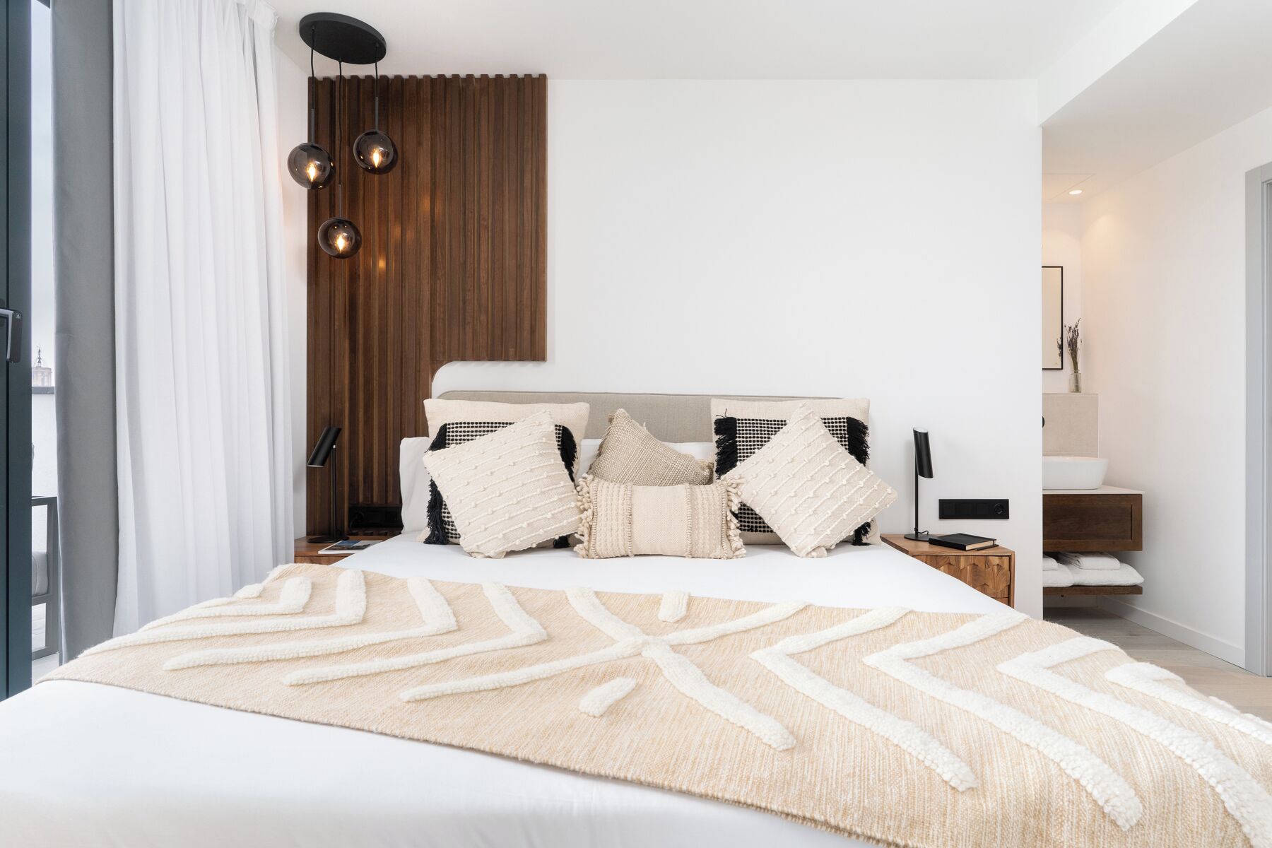 Un dormitorio moderno con una cama grande, varias almohadas, una mesita de noche y un panel de pared de madera.