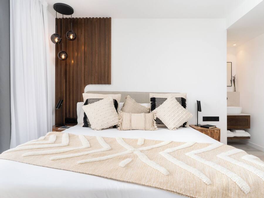 Un dormitorio moderno con una cama grande, varias almohadas, una mesita de noche y un panel de pared de madera.