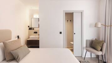 Una habitación de hotel moderna con una cama grande, una mesita de noche, una silla, un espejo y un baño visible a través de una puerta abierta.