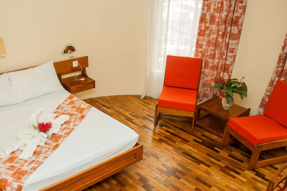 Une chambre d’hôtel avec un lit en bois, une table de chevet, une chaise rouge et une petite table sur laquelle se trouve une plante.