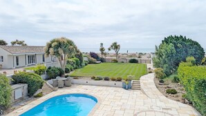 A pool area with a clear view of the ocean, a well-maintained lawn, and a patio with outdoor furniture. - A family house that sleeps 12 guests  in 6 bedrooms (Bognor Regis)