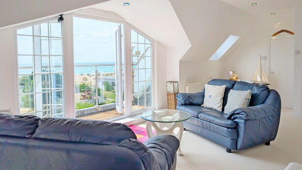 A spacious living room with a large glass door leading to a balcony with a view of the sea. - A family house that sleeps 12 guests  in 6 bedrooms (Bognor Regis)