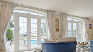 A spacious room with a large window, a blue sofa, and a view of a swimming pool. - A family house that sleeps 12 guests  in 6 bedrooms (Bognor Regis)