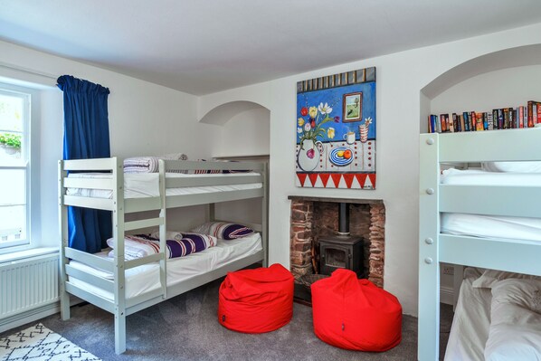 A bunk bed room with a fireplace, a bookshelf, and a window with curtains. - Woodleigh, Cawsand (Cawsand)