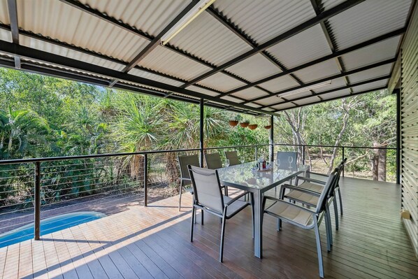 A covered outdoor dining area with a pool, surrounded by lush greenery.