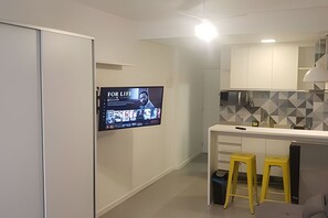 Une cuisine moderne avec un t éléviseur à écran plat fixé au mur, un plan de travail blanc et deux tabourets jaunes.