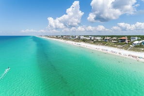 A coastal beach with clear turquoise waters, a sandy shore, and beachfront properties.
