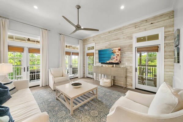 A spacious living room with a ceiling fan, a large TV, and a wooden accent wall.