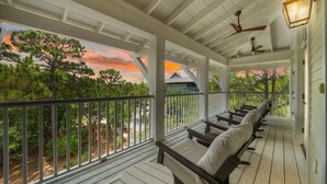 A covered porch with wooden railings, a ceiling fan, and a view of trees and houses.