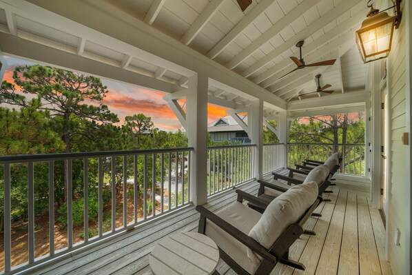 A covered porch with wooden railings, a ceiling fan, and a view of trees and houses.