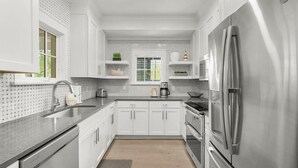 A modern kitchen with white cabinets, stainless steel appliances, and a window with blinds.