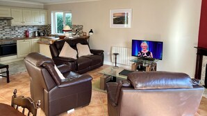 Ein modernes Wohnzimmer mit Ledersofas, einem Glastisch und einem Fernseher.