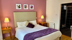 Ein ordentlich bezogenes Bett mit Kopfteil, zwei Nachttische mit Lampen, einer violetten Tagesdecke und drei gerahmten Bildern an der Wand.