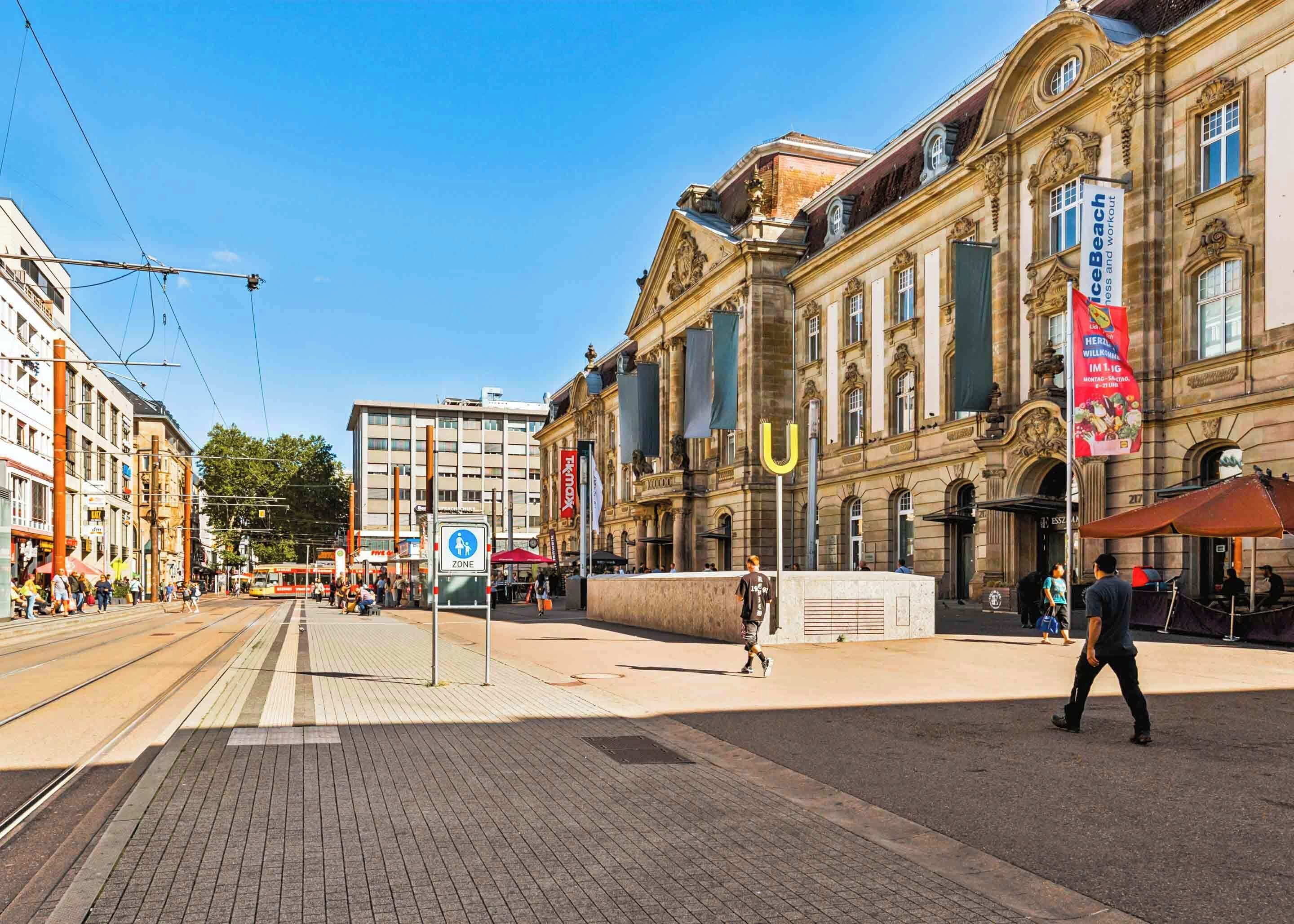 En historisk byggnad med klassisk arkitektur, en spårvagnslinje och en gågata.