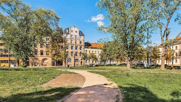 A park with a paved path, trees, and a building with multiple floors and windows.