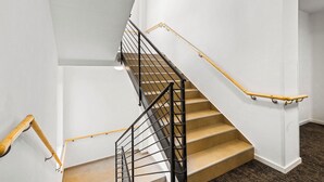 Una escalera con barandilla de metal negro y pasamanos de madera, que conduce a un piso superior.
