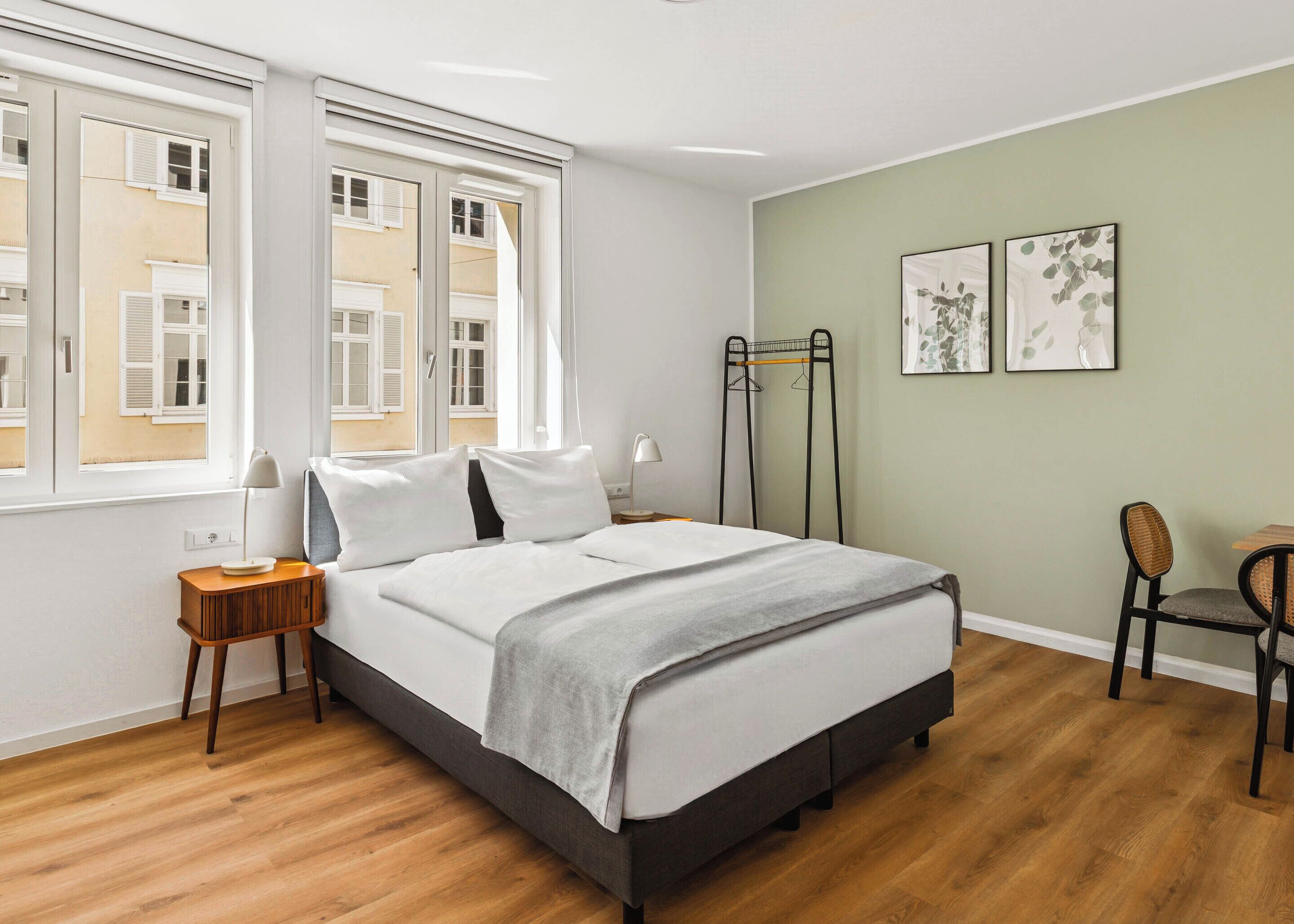 A neatly arranged bedroom with a bed, bedside tables, a chair, and artwork on the wall.