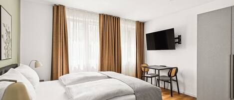 A modern hotel room with a large bed, a desk with a chair, a television mounted on the wall, and a wardrobe.