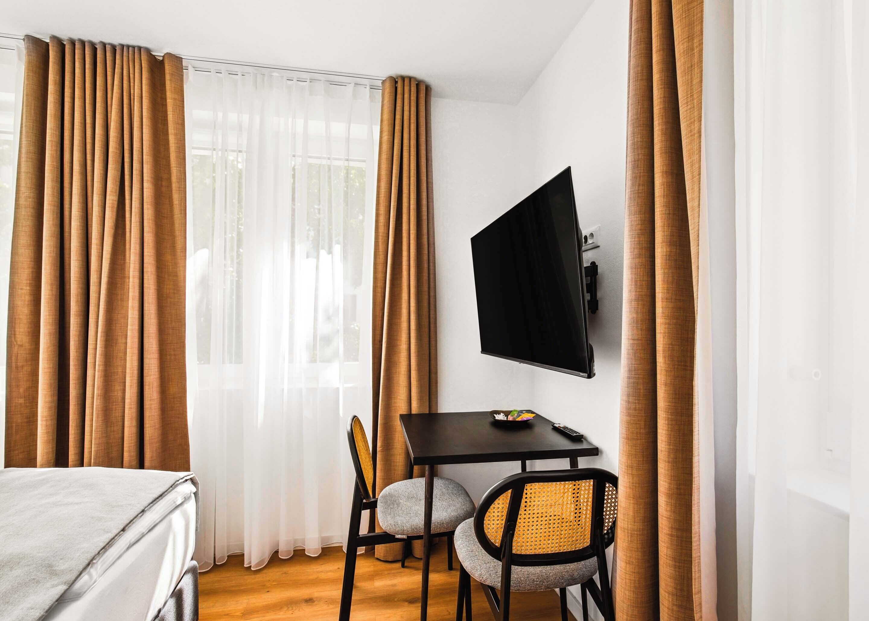 A hotel room with a bed, a desk with a TV, and two chairs.