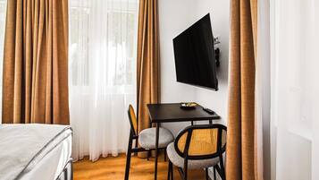 A hotel room with a bed, a desk with a TV, and two chairs.