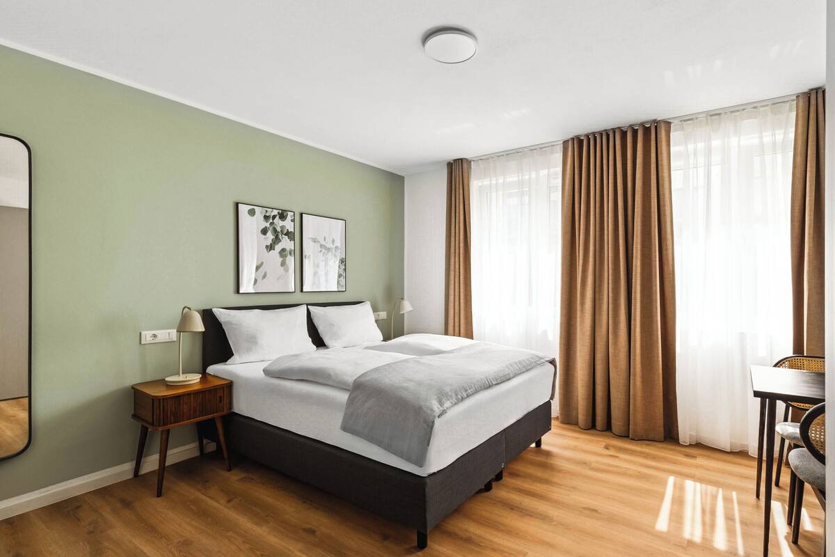 A modern hotel room with a large bed, a bedside table, a lamp, and a chair.