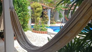 Una hamaca en un patio con piscina y diversas plantas.