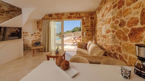 A cozy living room with stone walls, a sofa, a coffee machine, and a view of the outdoors. - Minoan Villas (Malia)
