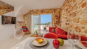 A dining area with a table set for two, a red sofa, and a view of the beach through a glass door. - Minoan Villas (Malia)