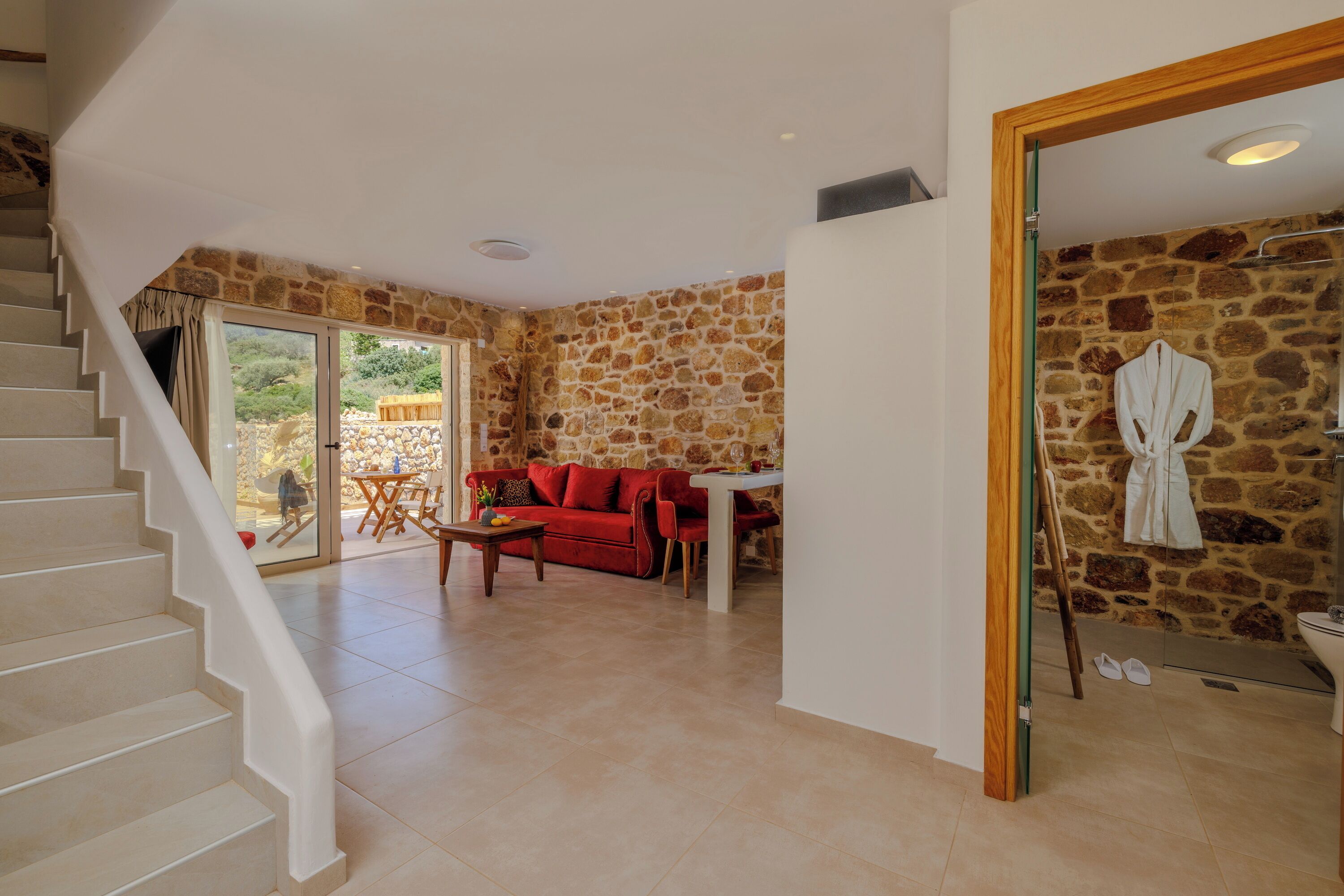 A spacious living area with a staircase, a red sofa, a dining table, and a stone wall.