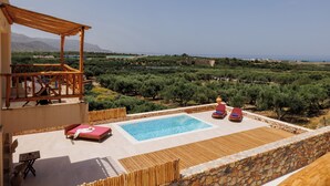 A rooftop pool with wooden deck, lounge chairs, and a pergola overlooking a vineyard and coastline. - Minoan Villas (Malia)