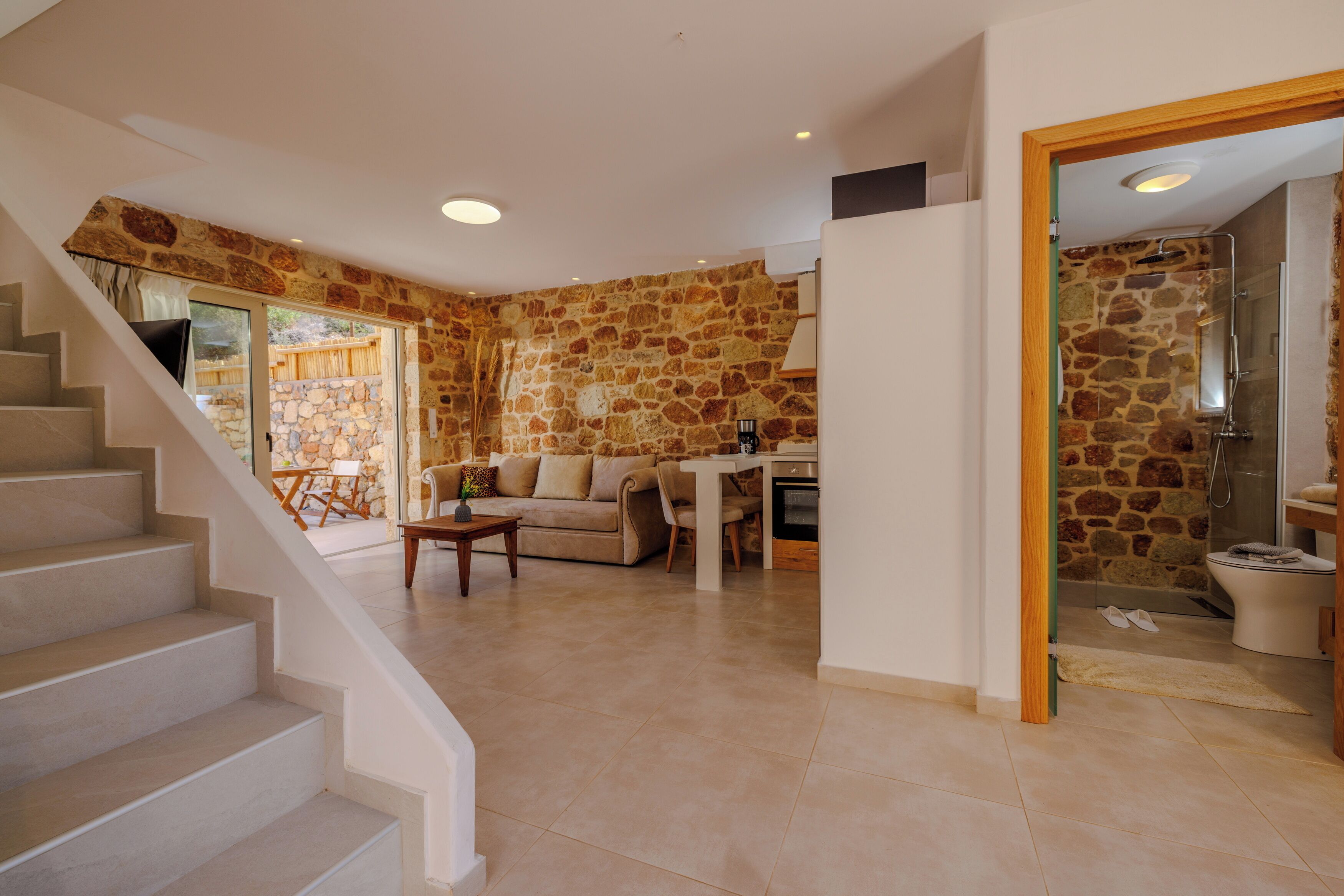 Amplia sala de estar con pared de piedra, una escalera, un sofá y una mesa de comedor.