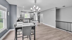 A spacious kitchen with modern appliances, a dining area with a wooden table, and a view of the outdoors through large windows. - Pet-friendly Getaway With Golf & Private Patio Retreat 4 Bedroom Home (South Bend)