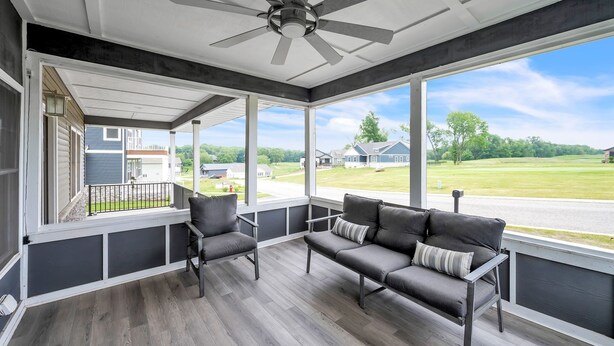 A covered porch with a ceiling fan, two chairs, a sofa, and large windows offering a view of a green landscape and neighboring houses. - Pet-friendly Getaway With Golf & Private Patio Retreat 4 Bedroom Home (South Bend)