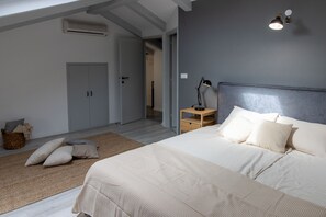 Et soveværelse med en stor seng, et natbord med en lampe, et garderobeskab og en dør til et andet rum.
