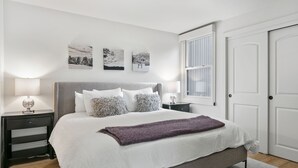 Un dormitorio ordenado con una cama grande, dos mesitas de noche y un ventanal.