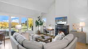 Amplia sala de estar con chimenea, televisor montado encima y un gran ventanal con vista a un campo de golf.