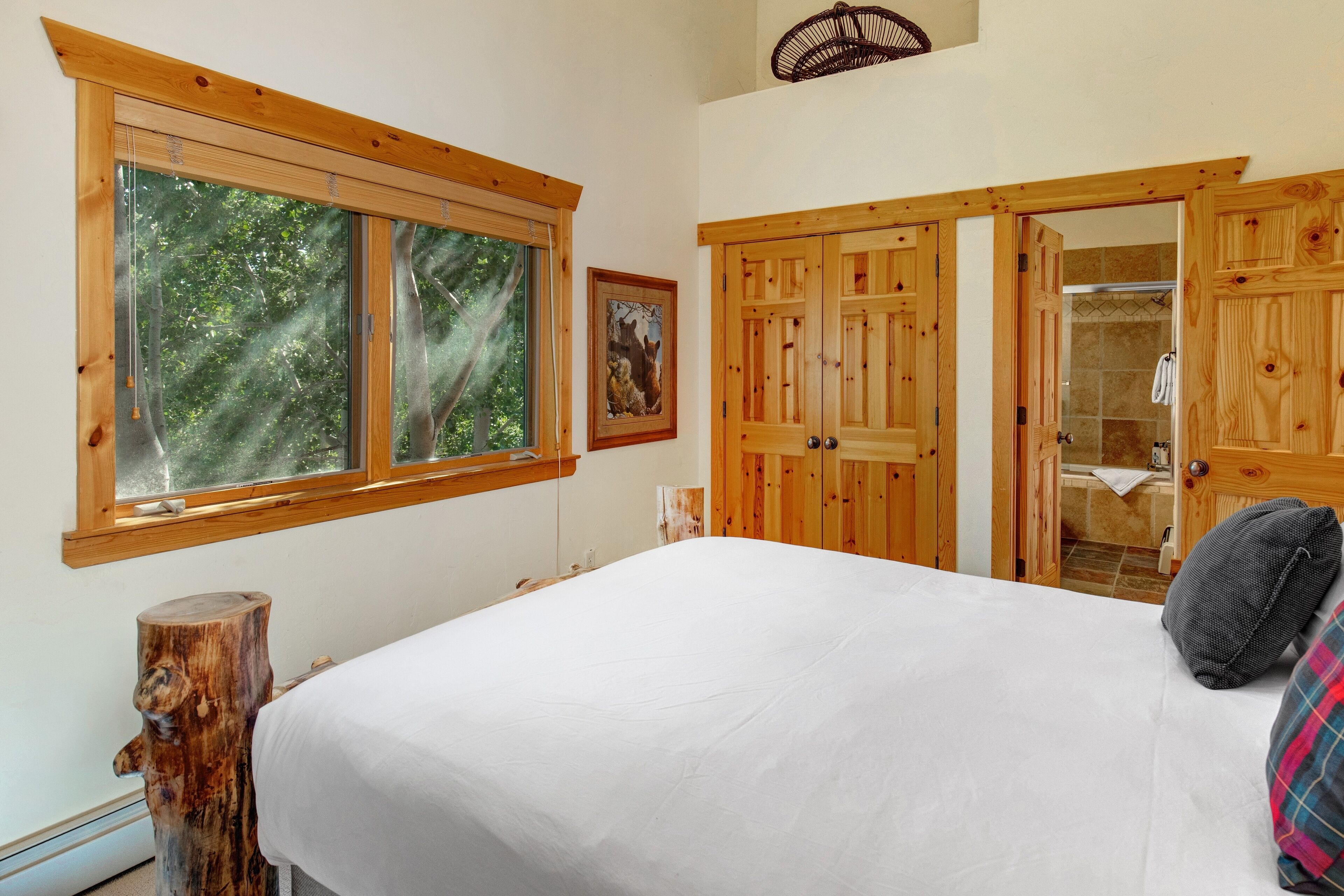 Une chambre avec un grand lit, une armoire en bois et une fenêtre donnant sur les arbres.